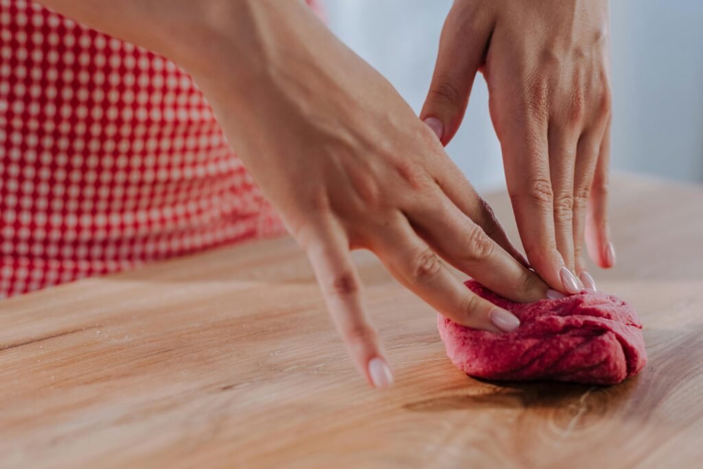 Close-up of female hands kneading vibrant red dough on a wooden surface, showcasing pasta preparation.