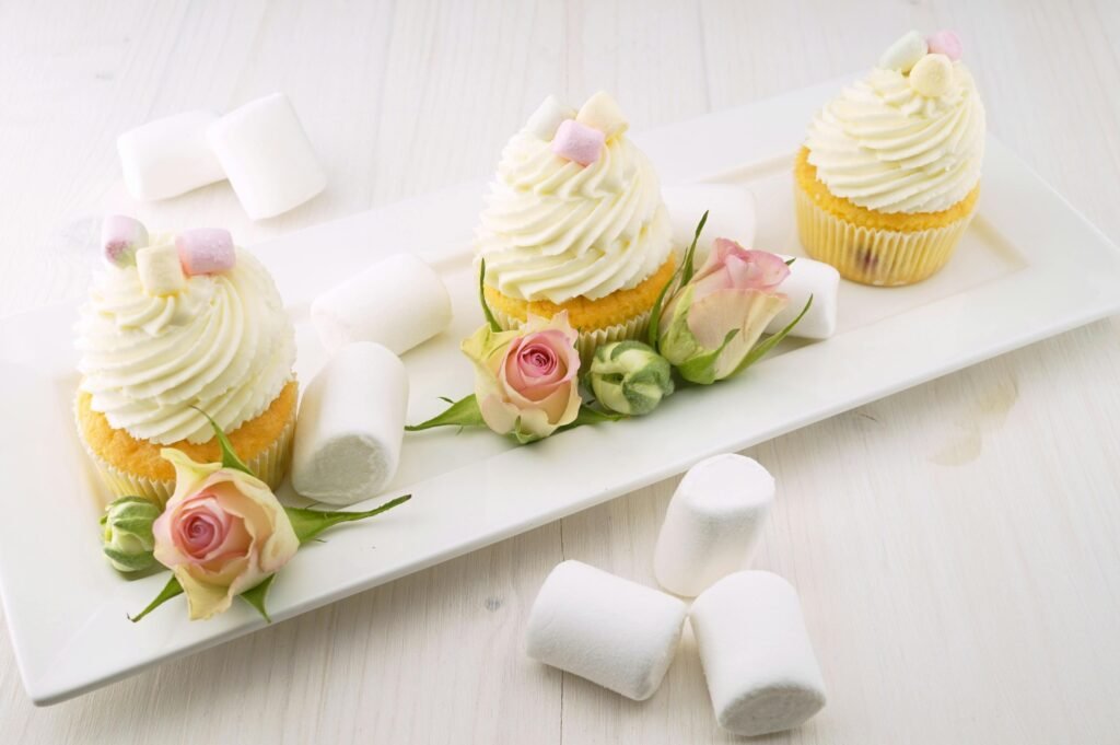 Vanilla cupcakes adorned with roses and fluffy marshmallows create a tempting treat.