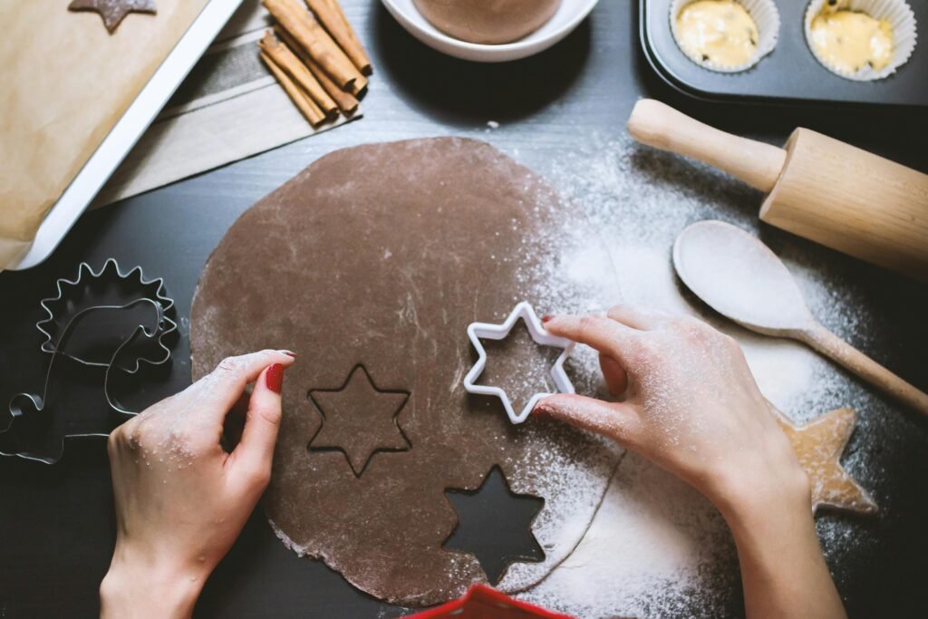 Hands cutting star-shaped cookies from chocolate dough, surrounded by baking tools.